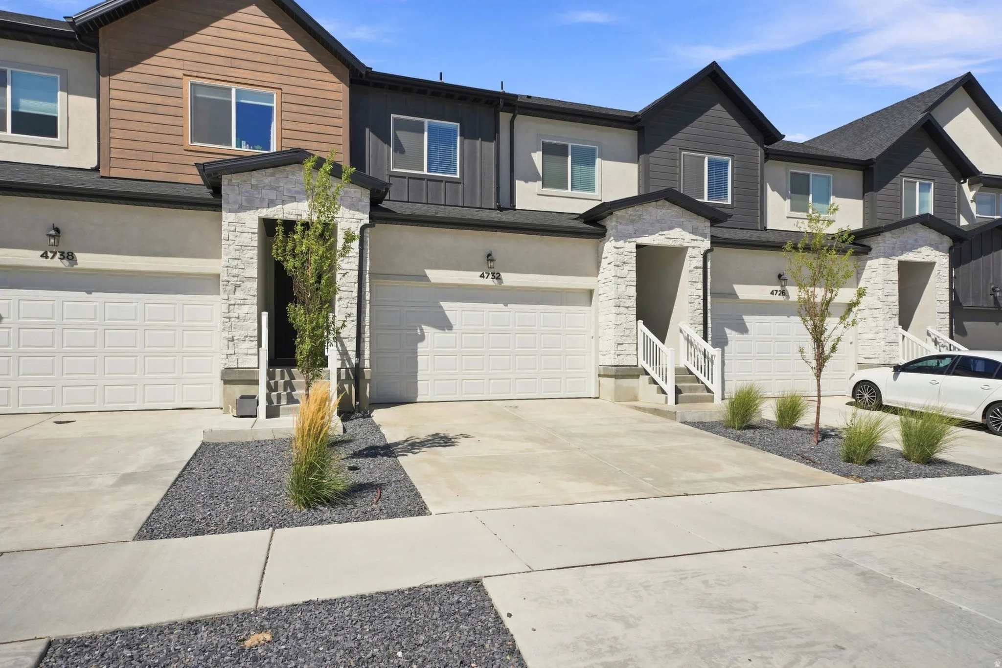 Two-story facade with stone veneer accents, individual garage doors, and low-maintenance landscaping