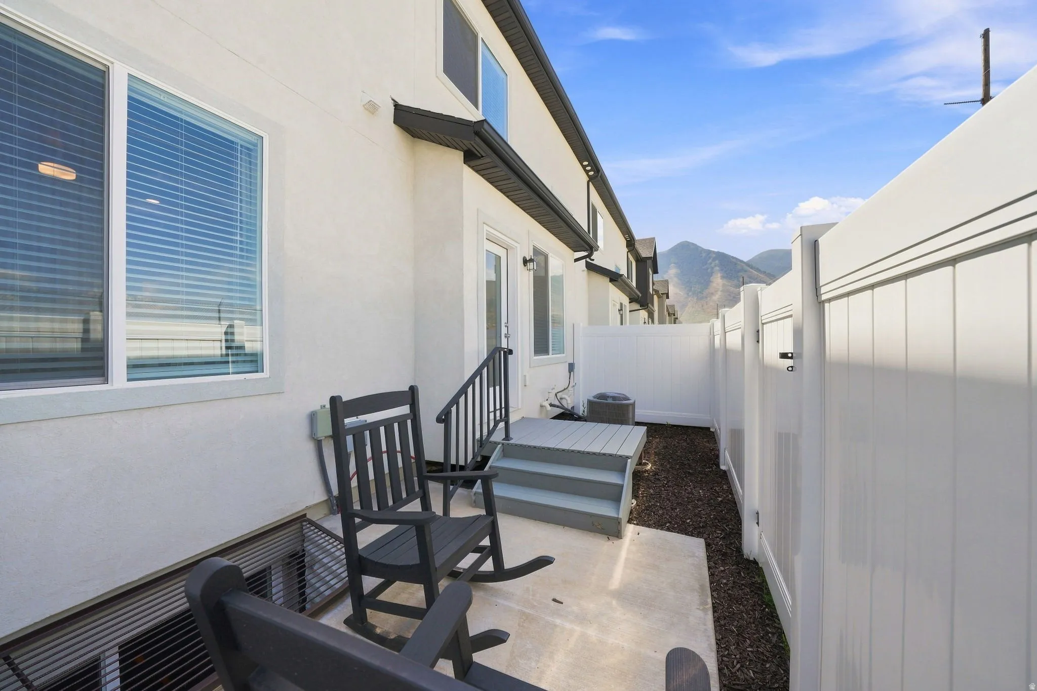 Private patio with concrete flooring, elevated deck access, and white vinyl fencing