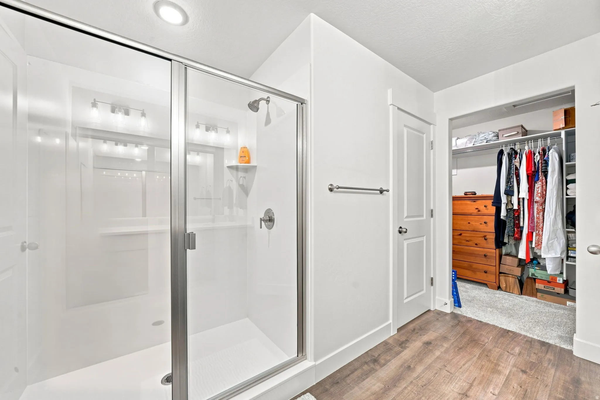 Enclosed shower with clear glass door, brushed nickel fixtures, recessed ceiling light, and wood-finish flooring