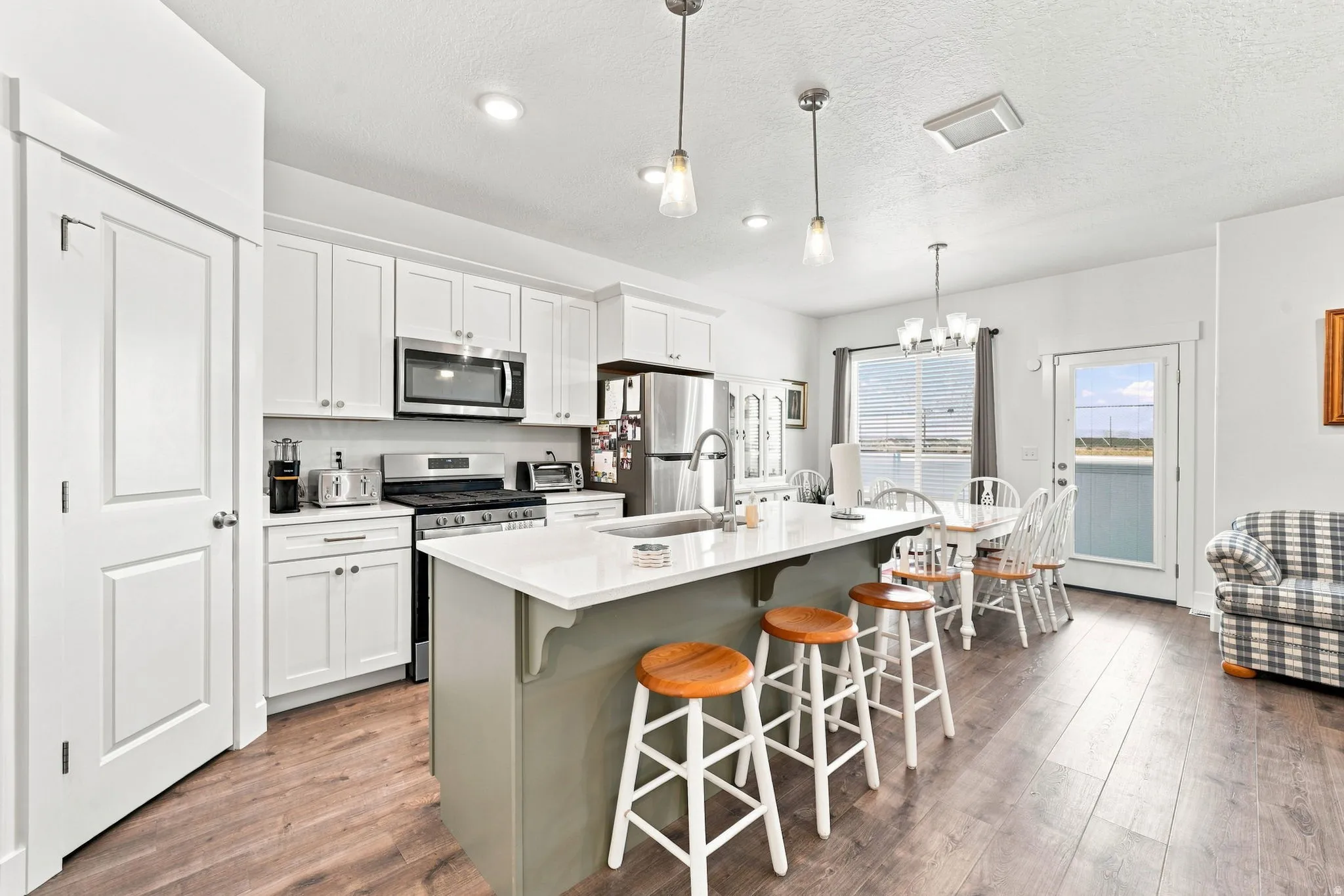 Kitchen featuring a central island with countertop seating, white shaker-style cabinetry, stainless steel appliances, and wood-finish flooring