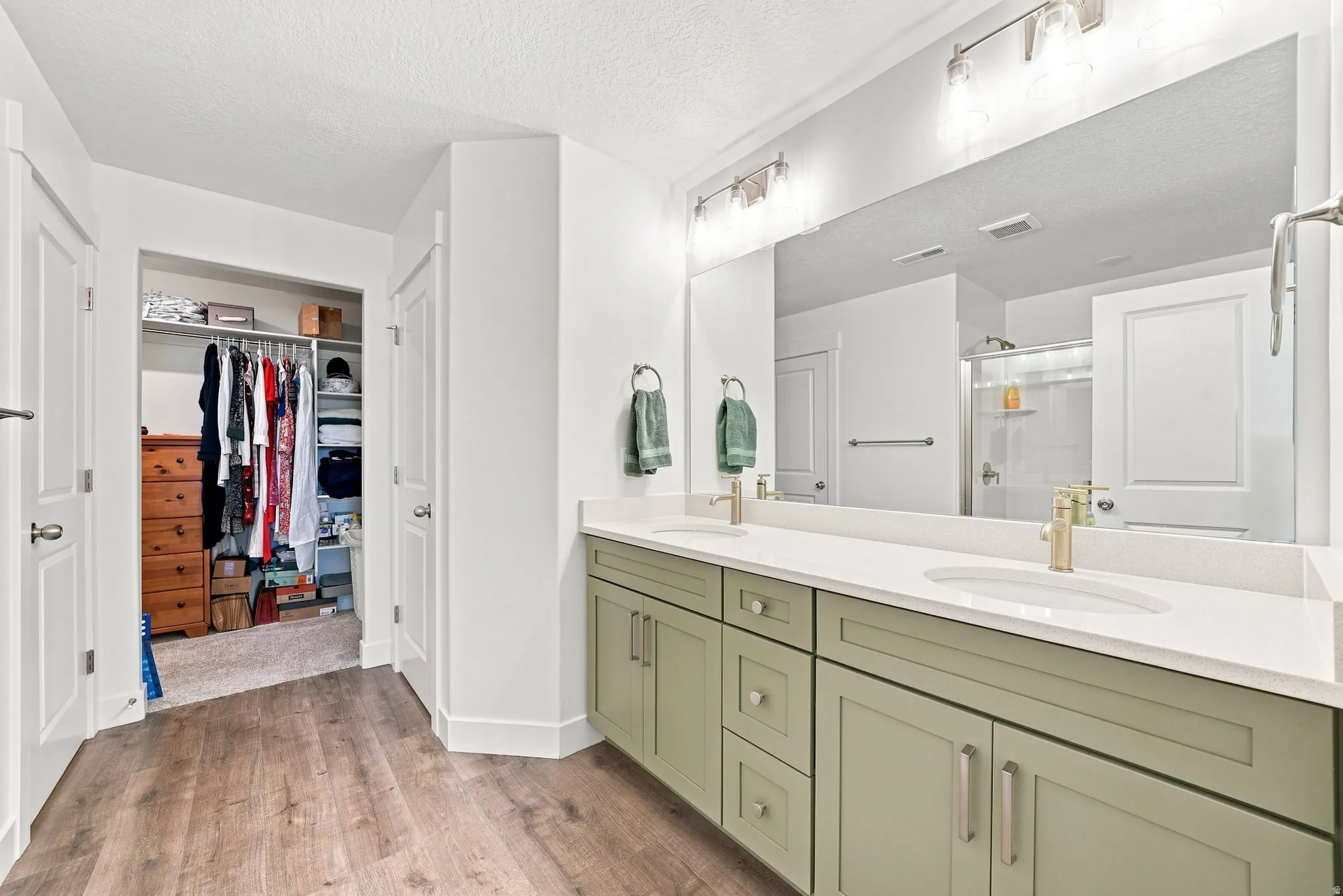 Dual vanity with light green cabinetry, white countertops, and gold-finish fixtures