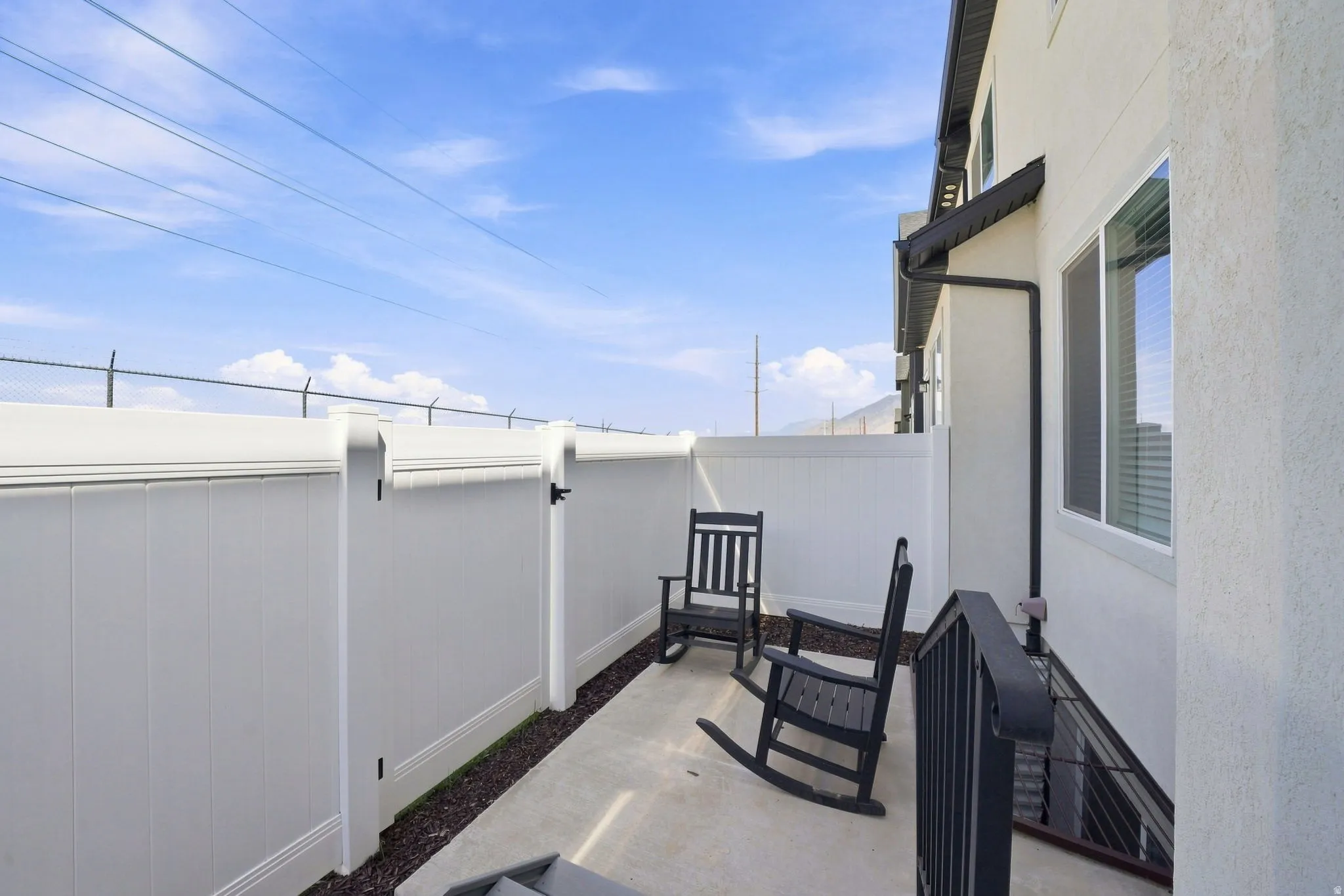 Paved patio area featuring white privacy fencing, a gate, and exterior wall siding