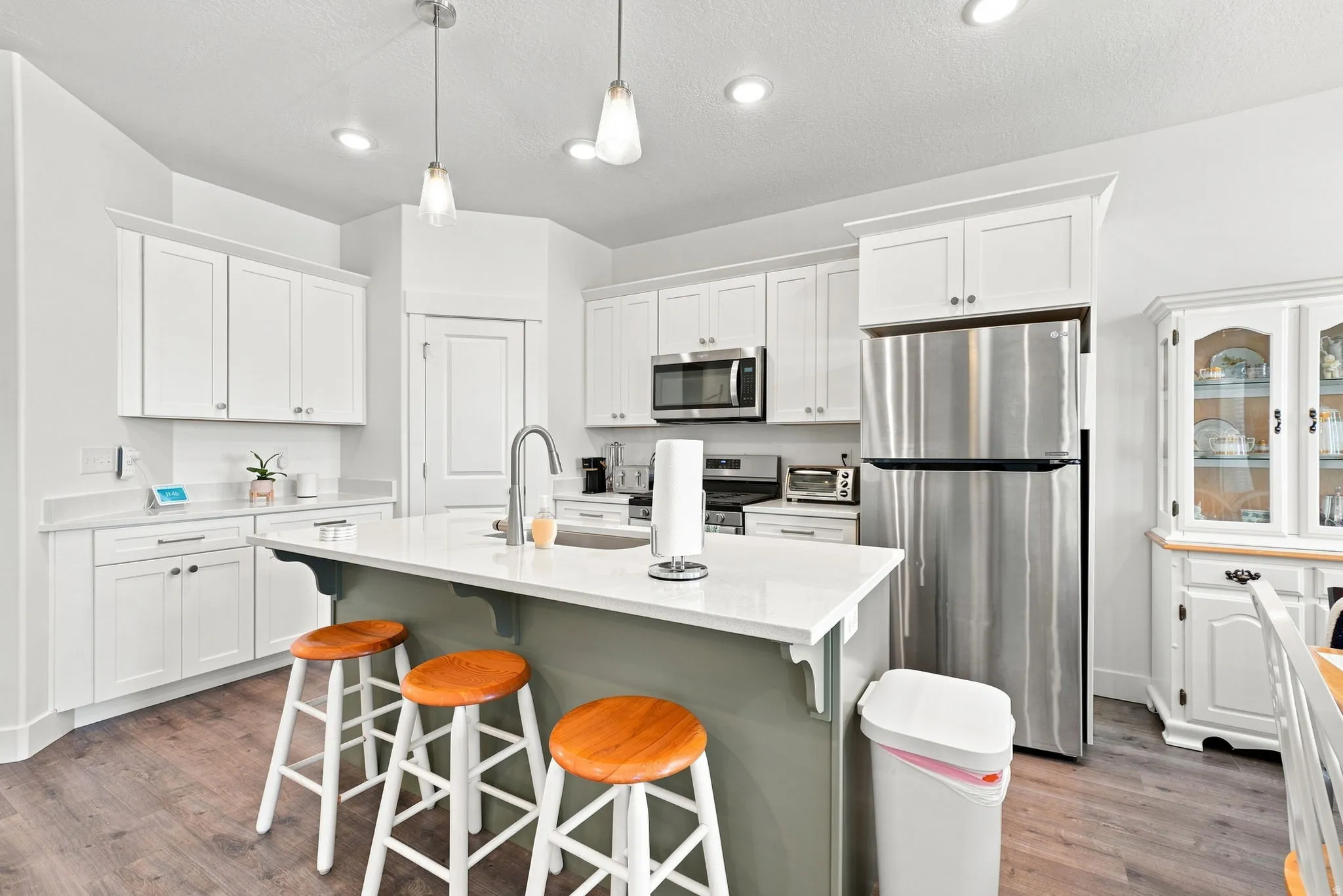 Kitchen featuring white cabinetry, stainless steel appliances, an island with seating, a stainless steel sink with a gooseneck faucet, and wood-finish flooring