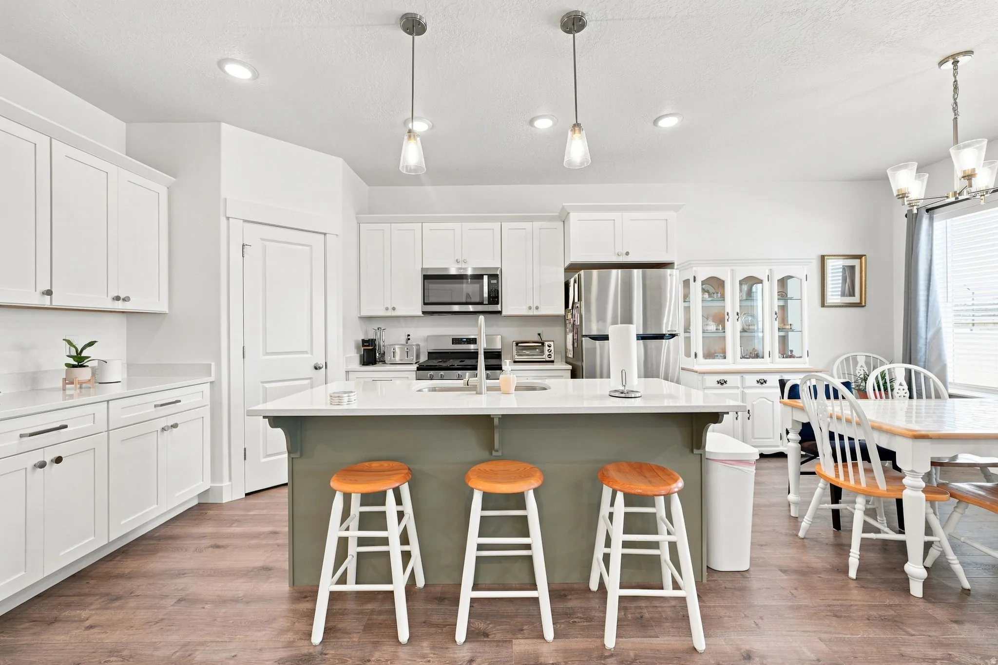 Spacious kitchen featuring white cabinetry, light countertops, wood-finish flooring, and a large center island with pendant lighting