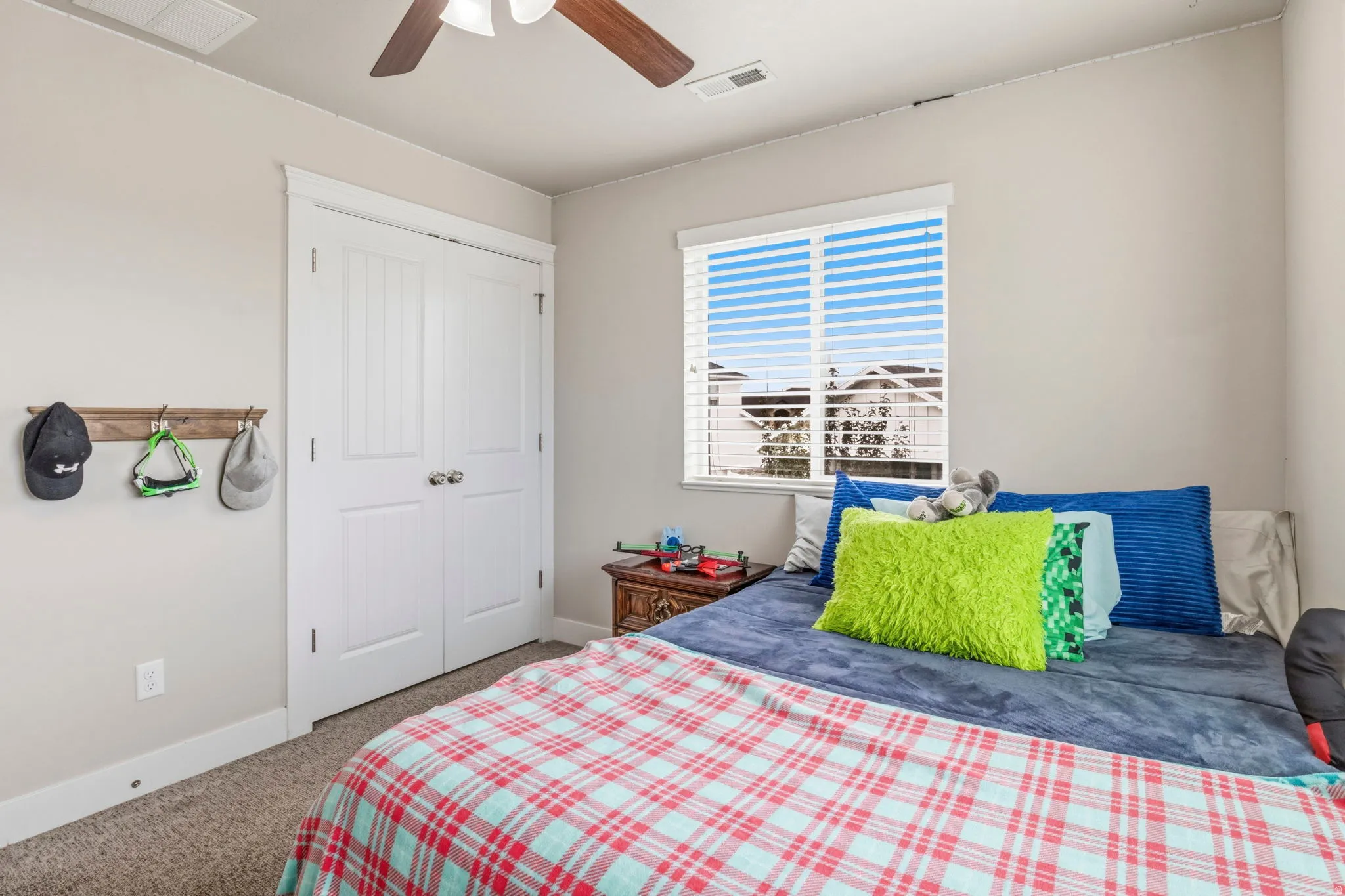Carpeted flooring, a window with blinds, a ceiling fan, and white paneled bi-fold doors