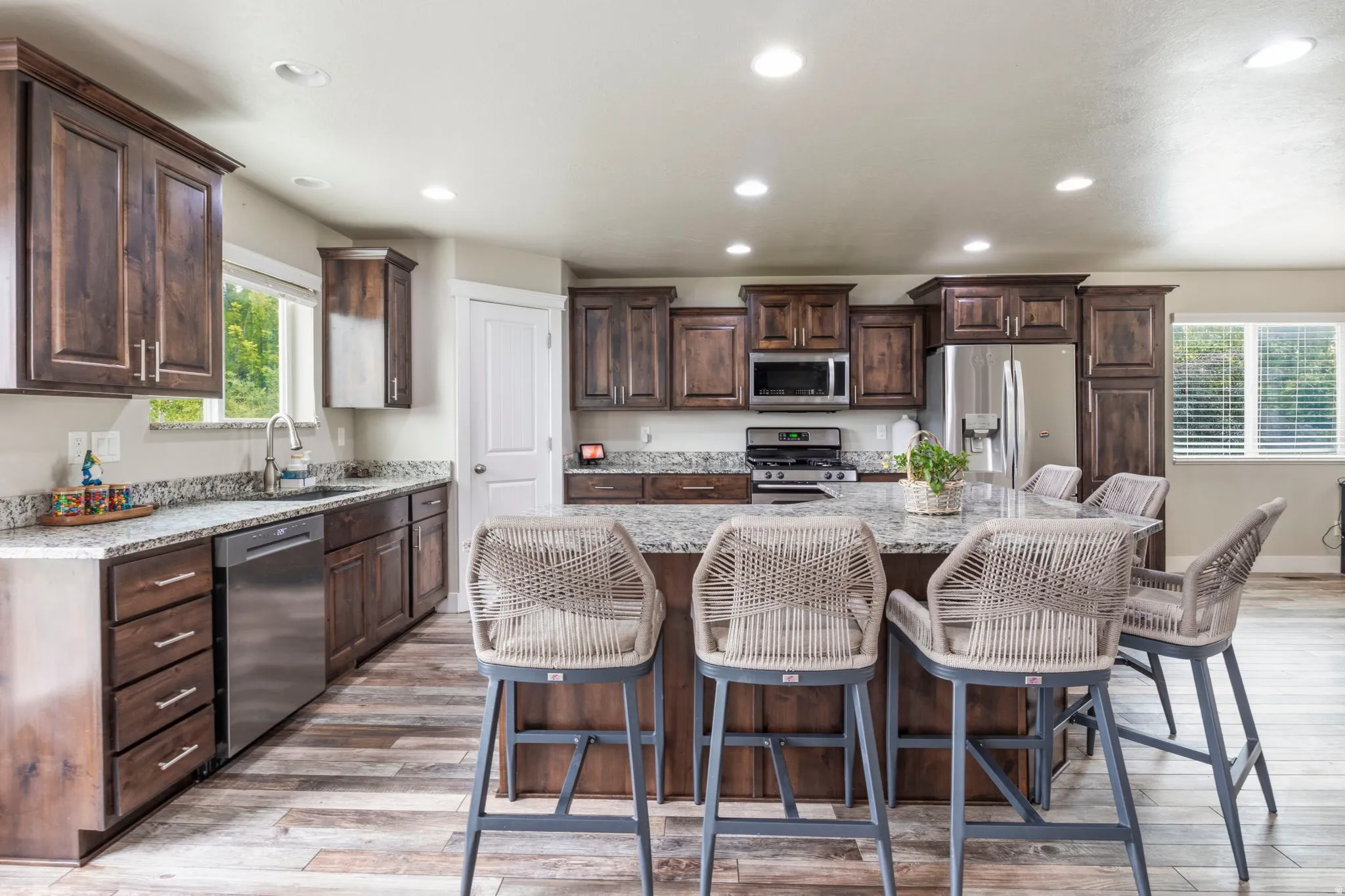 Spacious kitchen featuring dark wood cabinetry, light-toned countertops, stainless steel appliances, a large center island, and wood-finish flooring