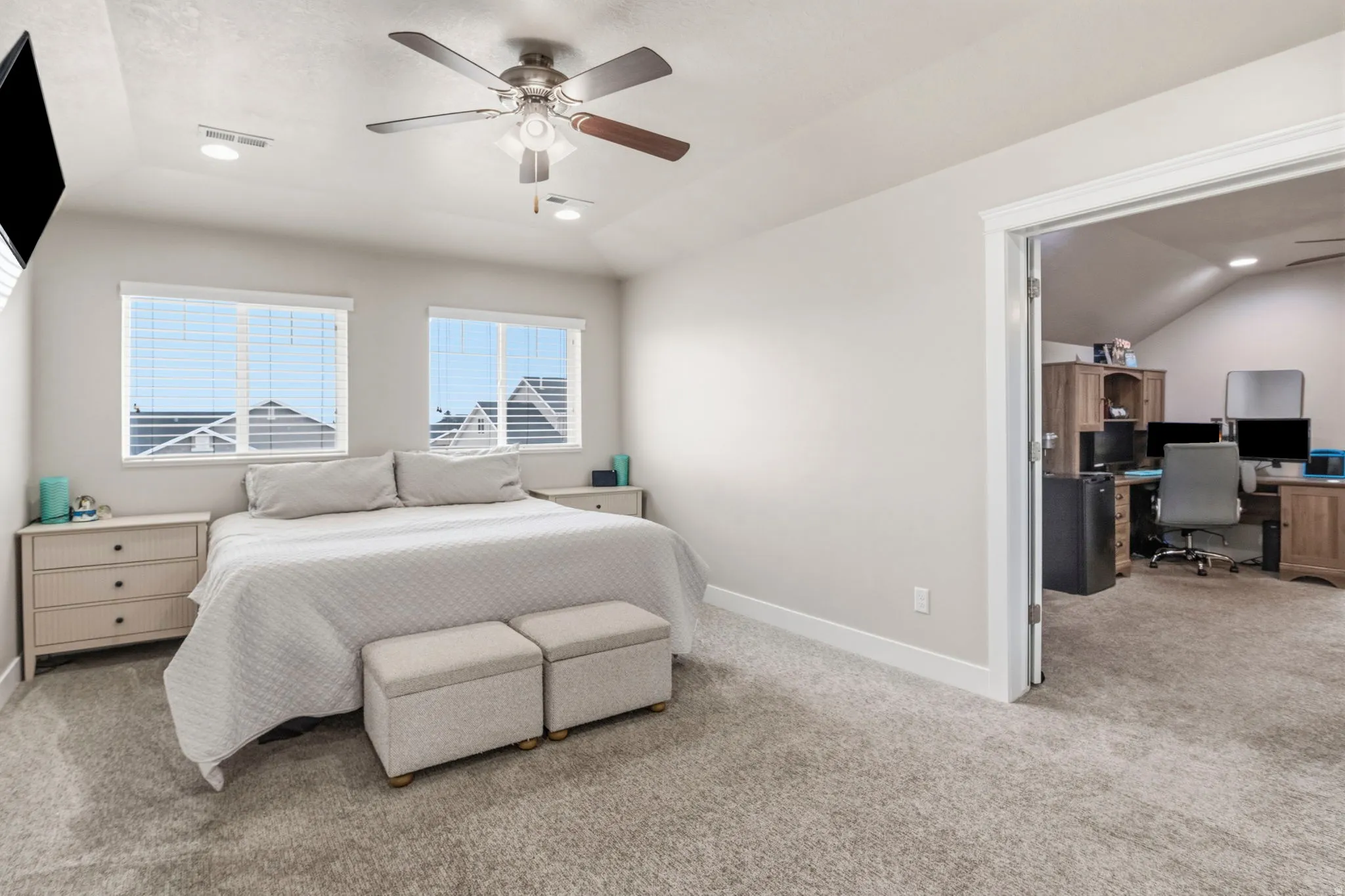 Recessed ceiling lights, ceiling fan, carpeting, two windows with horizontal blinds, and a doorway opening to another room