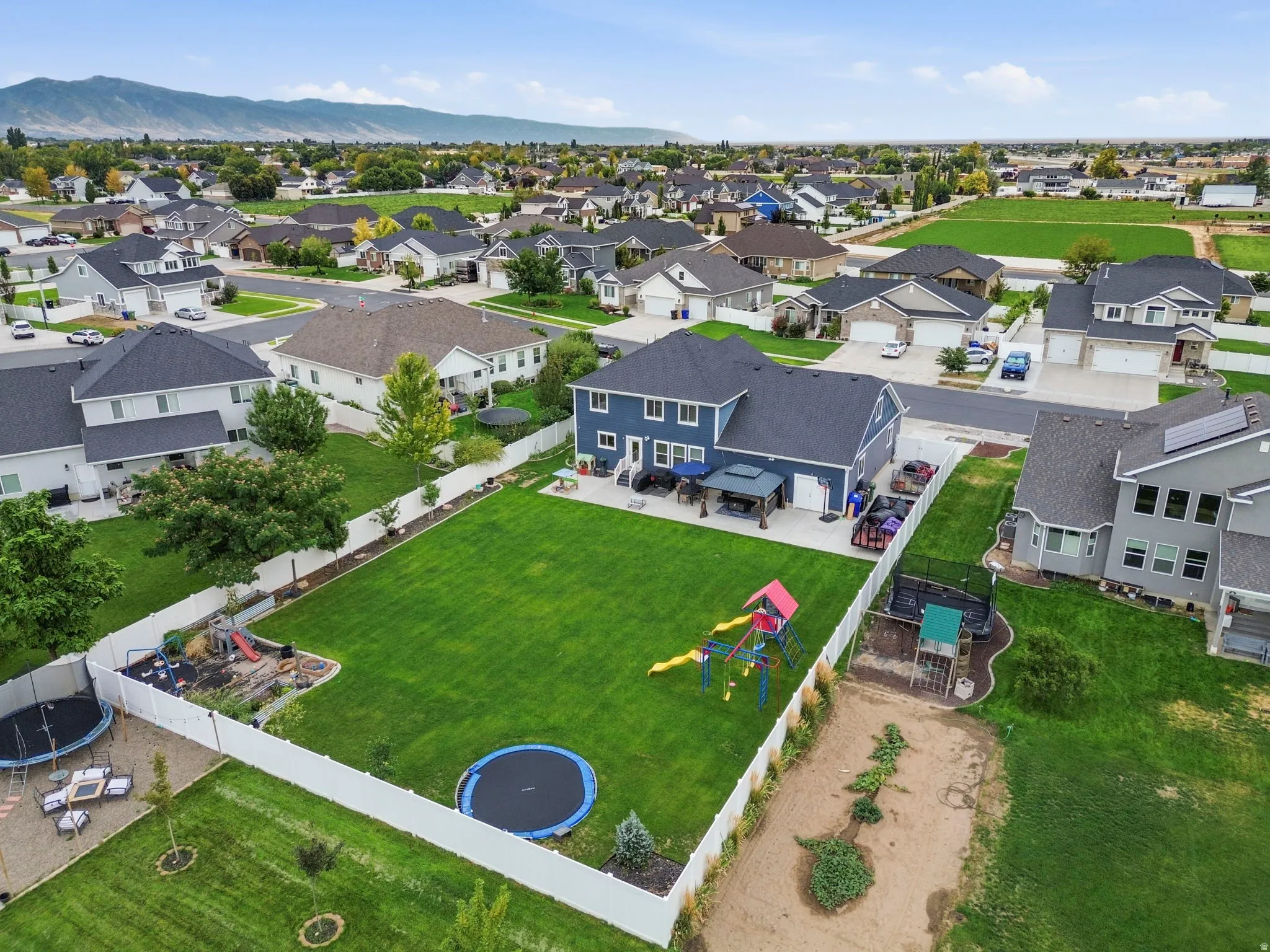 Expansive backyard with a manicured lawn, white privacy fencing, and a covered patio area