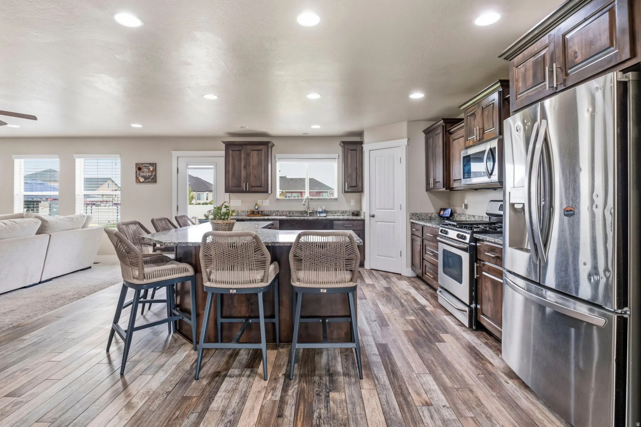 Spacious kitchen featuring an extended island with seating, stainless steel appliances, dark wood-finish cabinetry, light-toned countertops, and wood-finish flooring