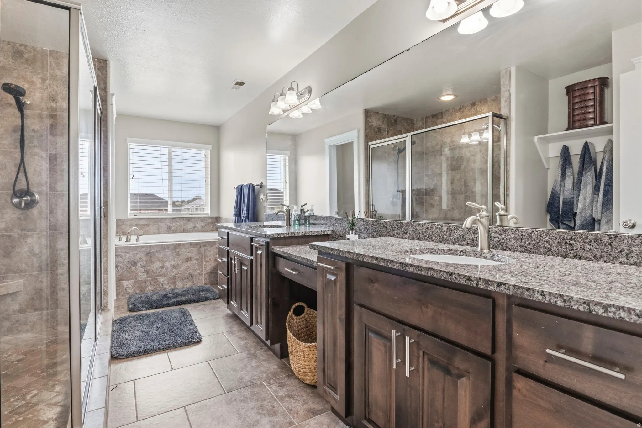 Dual vanity with stone countertops and undermount sinks, glass-enclosed shower, built-in bathtub, and tile flooring
