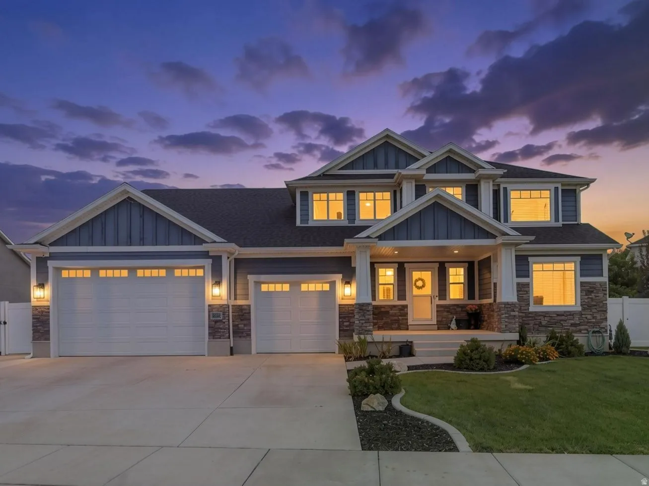 Two-story exterior with multi-toned siding and stone accents, featuring a covered entry, multiple windows, and a concrete driveway leading to two garage doors