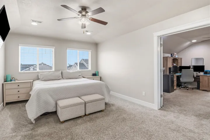 Recessed ceiling lights, ceiling fan, carpeting, two windows with horizontal blinds, and a doorway opening to another room