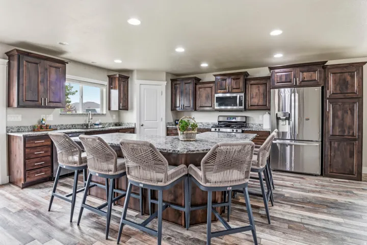 Spacious kitchen featuring an octagonal island, wood-finish flooring, dark wood cabinetry, granite countertops, and stainless steel appliances