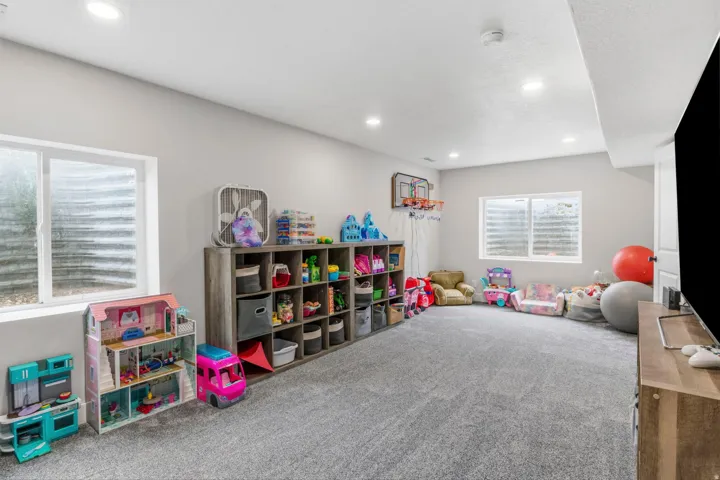 Spacious lower-level room featuring light gray carpeting, recessed lighting, and two windows