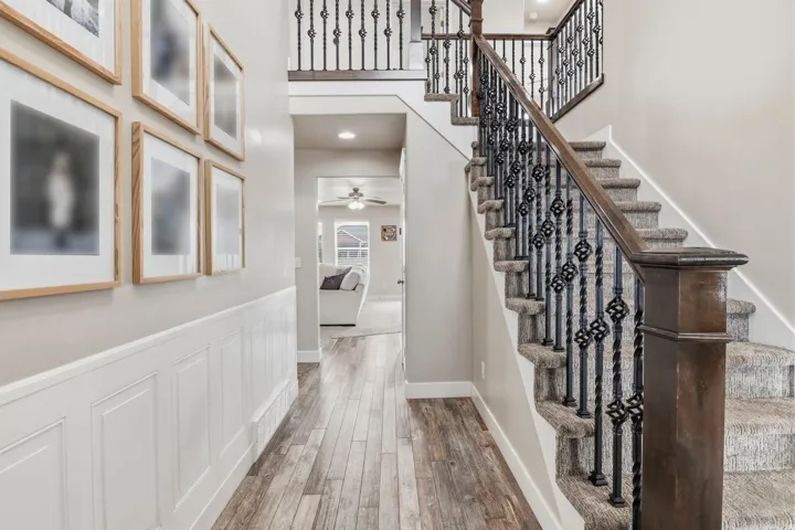 Staircase featuring decorative wrought iron balusters, wood-finish handrail, and carpeted treads