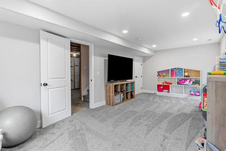 Spacious room with recessed lighting, light gray walls, gray patterned carpeting, and a white interior door