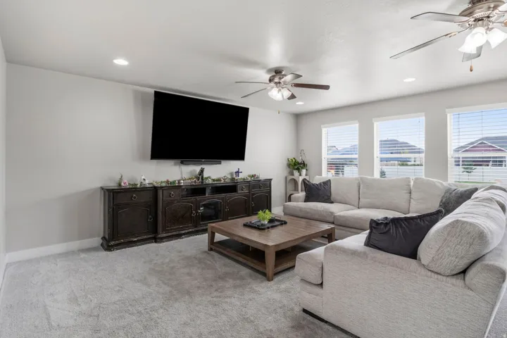 Recessed lighting, light gray wall color, two ceiling fans with integrated lighting, wood-finish media console, and a series of three windows