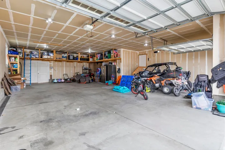 Expansive garage with concrete flooring, multiple overhead lighting fixtures, and integrated overhead storage shelving