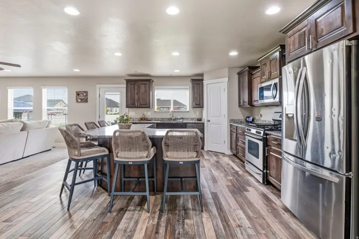 Spacious kitchen featuring an extended island with seating, stainless steel appliances, dark wood-finish cabinetry, light-toned countertops, and wood-finish flooring