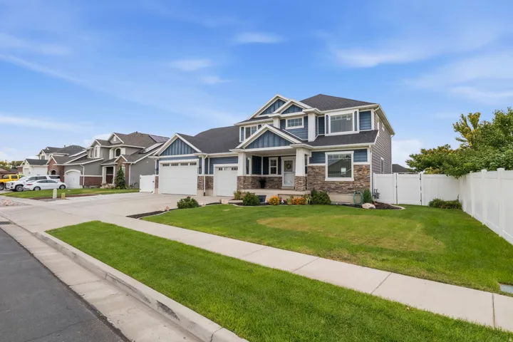 Two-story exterior with stone and siding accents, dual garage doors, a white privacy fence, and a manicured lawn
