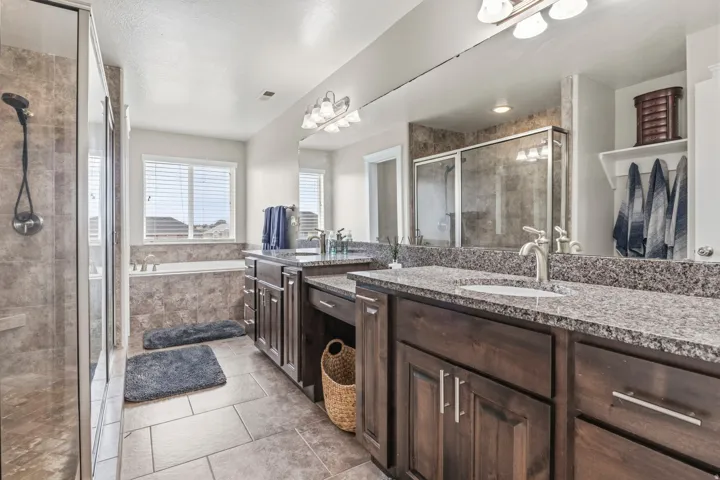 Dual vanity with stone countertops and undermount sinks, glass-enclosed shower, built-in bathtub, and tile flooring