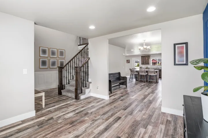Wood-finish flooring throughout, staircase with carpeted treads and wrought iron balusters, recessed lighting, and wainscoting paneling
