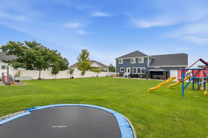 Expansive backyard featuring a manicured lawn, a white privacy fence, and mature trees
