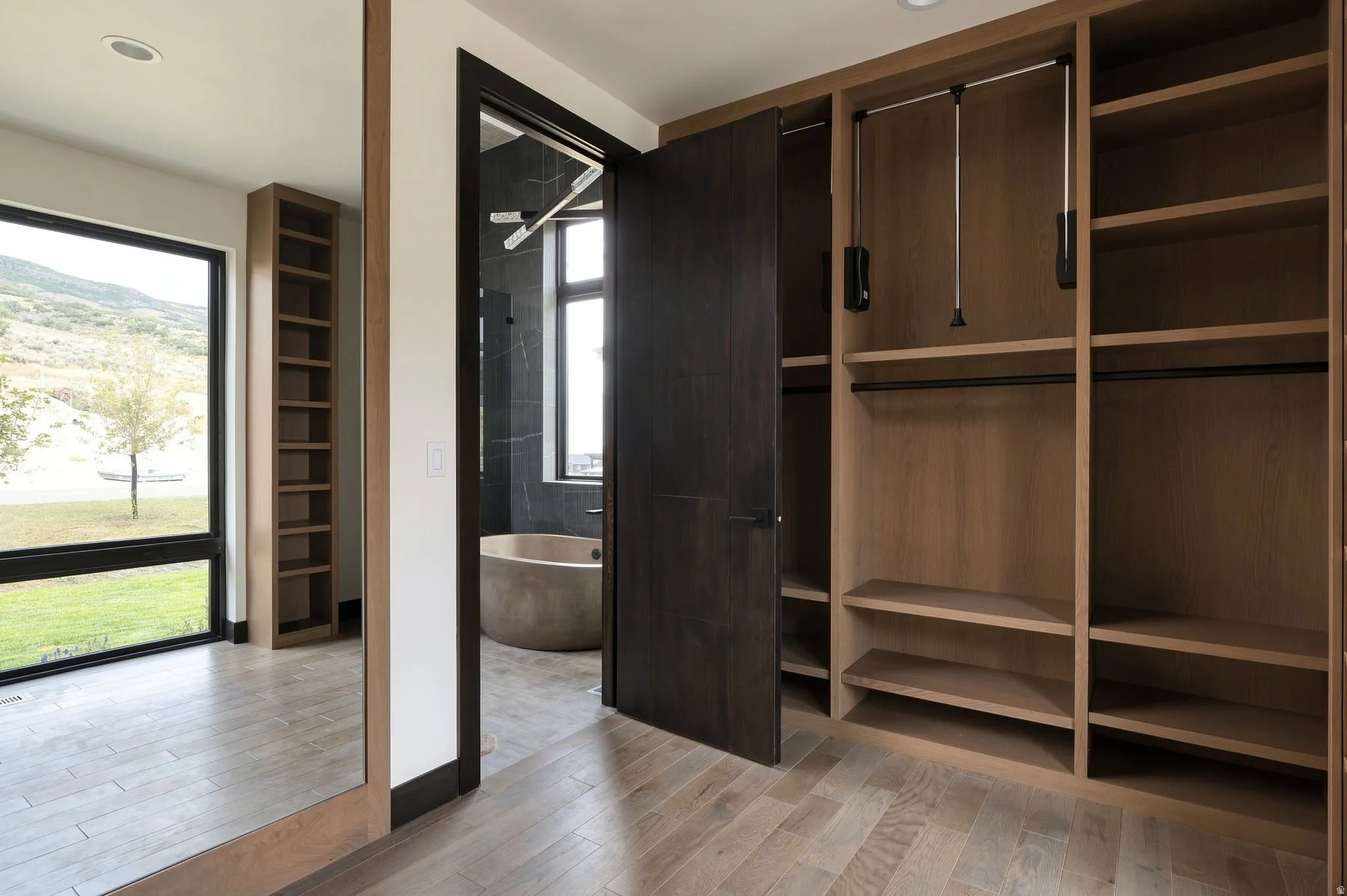 Built-in closet system with shelving and hanging rods, wood-finish flooring, full-length mirror, built-in shelving unit, and large window