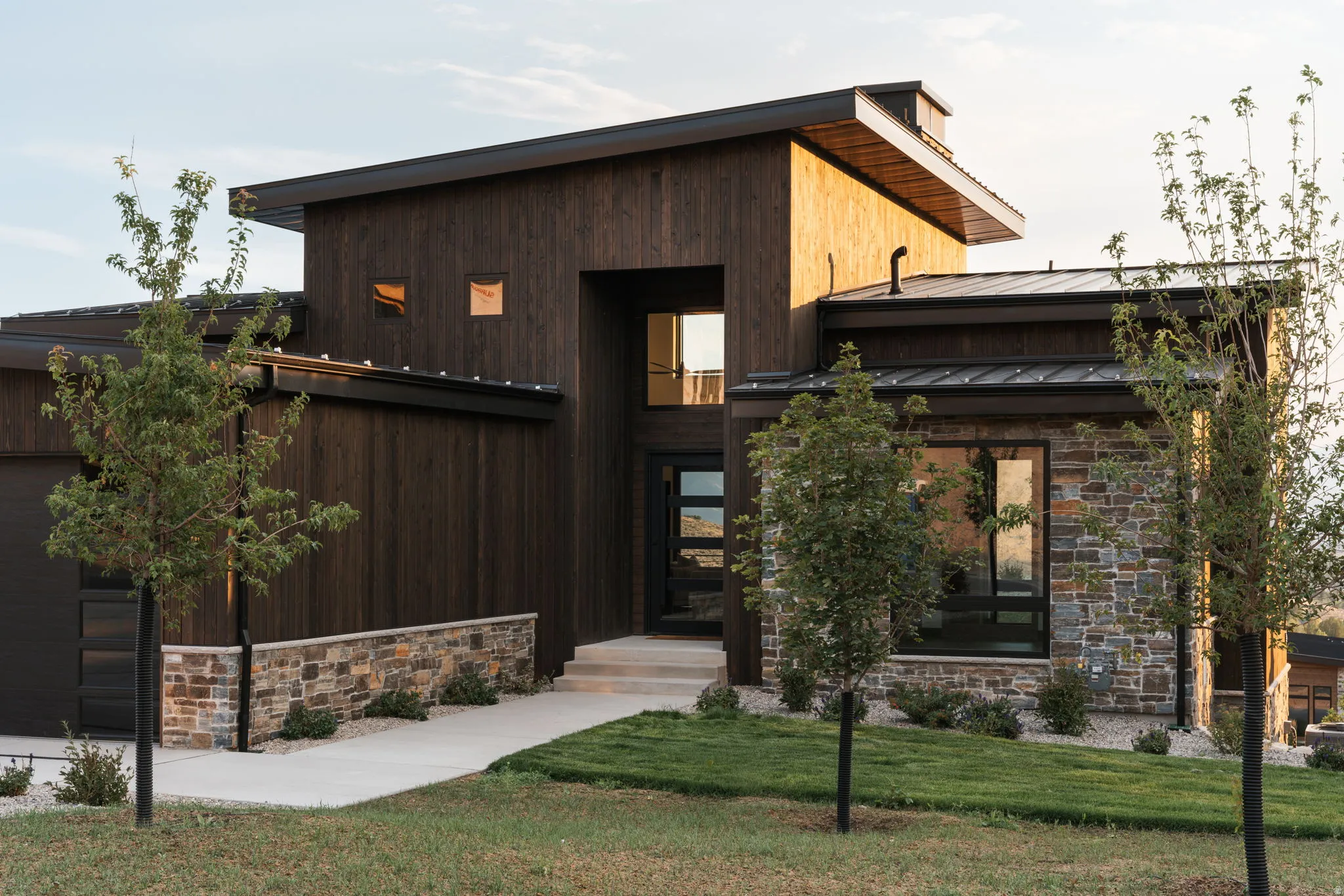 Contemporary exterior featuring dark wood siding, stone accents, a multi-pane glass entry door, and a metal roof