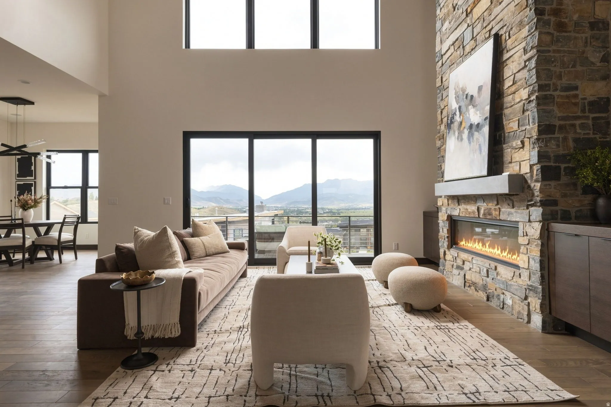 Soaring ceilings with upper transom windows, a stone fireplace with a linear insert, and wood-finish flooring