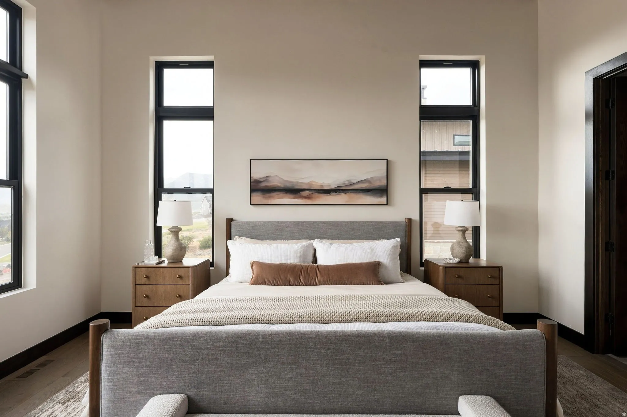 Tall black-framed windows, light wood-finish flooring, and a dark-stained interior door frame