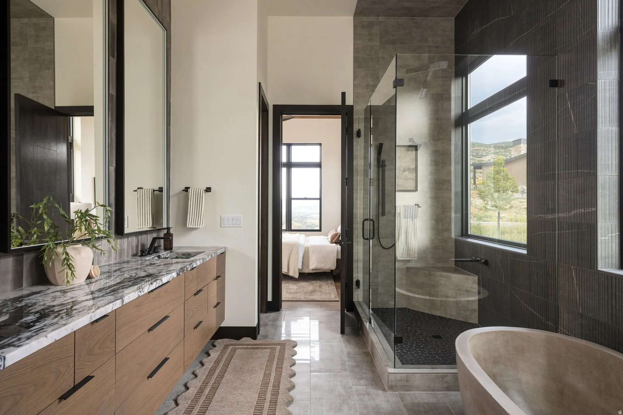 Dual vanity with a stone countertop, built-in soaking tub, glass-enclosed shower, and large windows