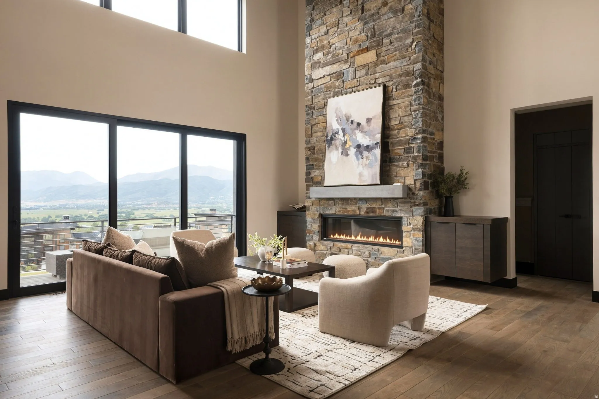 Soaring ceilings with transom windows, stone-clad fireplace with a linear gas insert, wood-finish flooring, and large sliding glass doors opening to a balcony