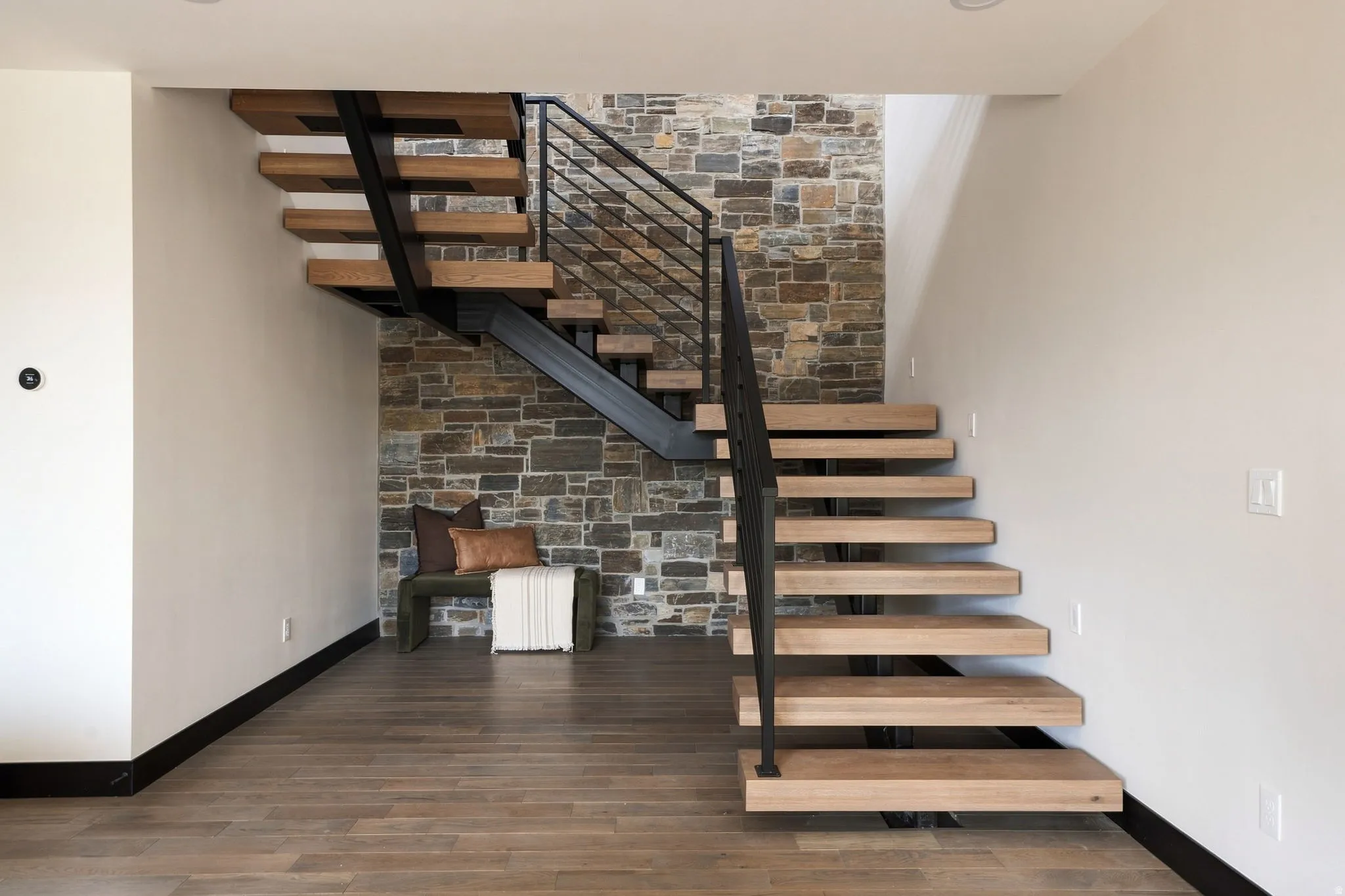 Floating wood staircase with black metal railing, stone accent wall, wood-finish flooring, and recessed lighting