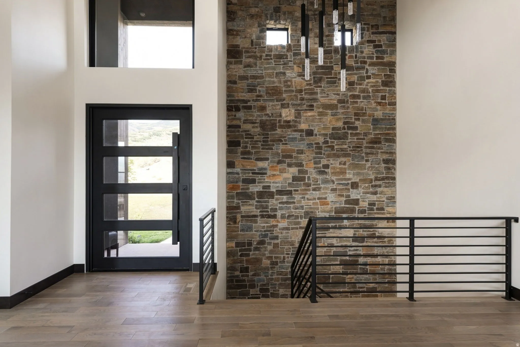 Entry foyer featuring a stone accent wall, wood-finish flooring, and a modern black entry door with frosted glass panels