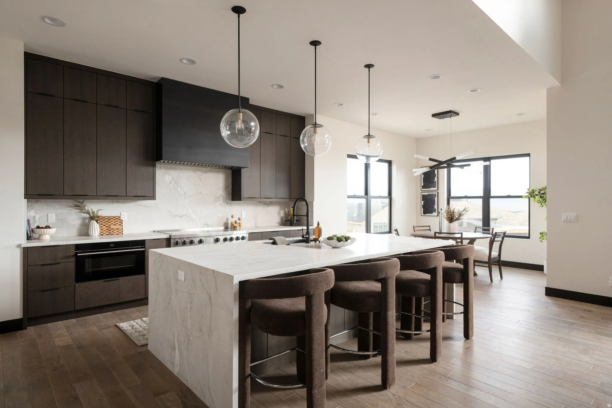 Spacious kitchen featuring dark wood-finish cabinetry, a waterfall island, stainless steel range, integrated wall oven, and wood-finish flooring