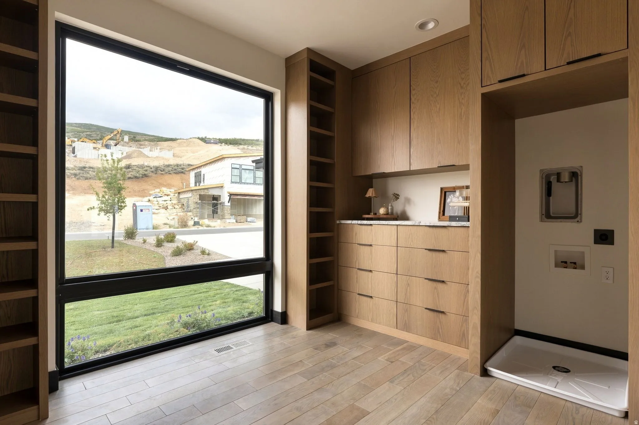 Expansive floor-to-ceiling window, wood-finish flooring, built-in wooden cabinetry, integrated shelving, and a built-in utility pan