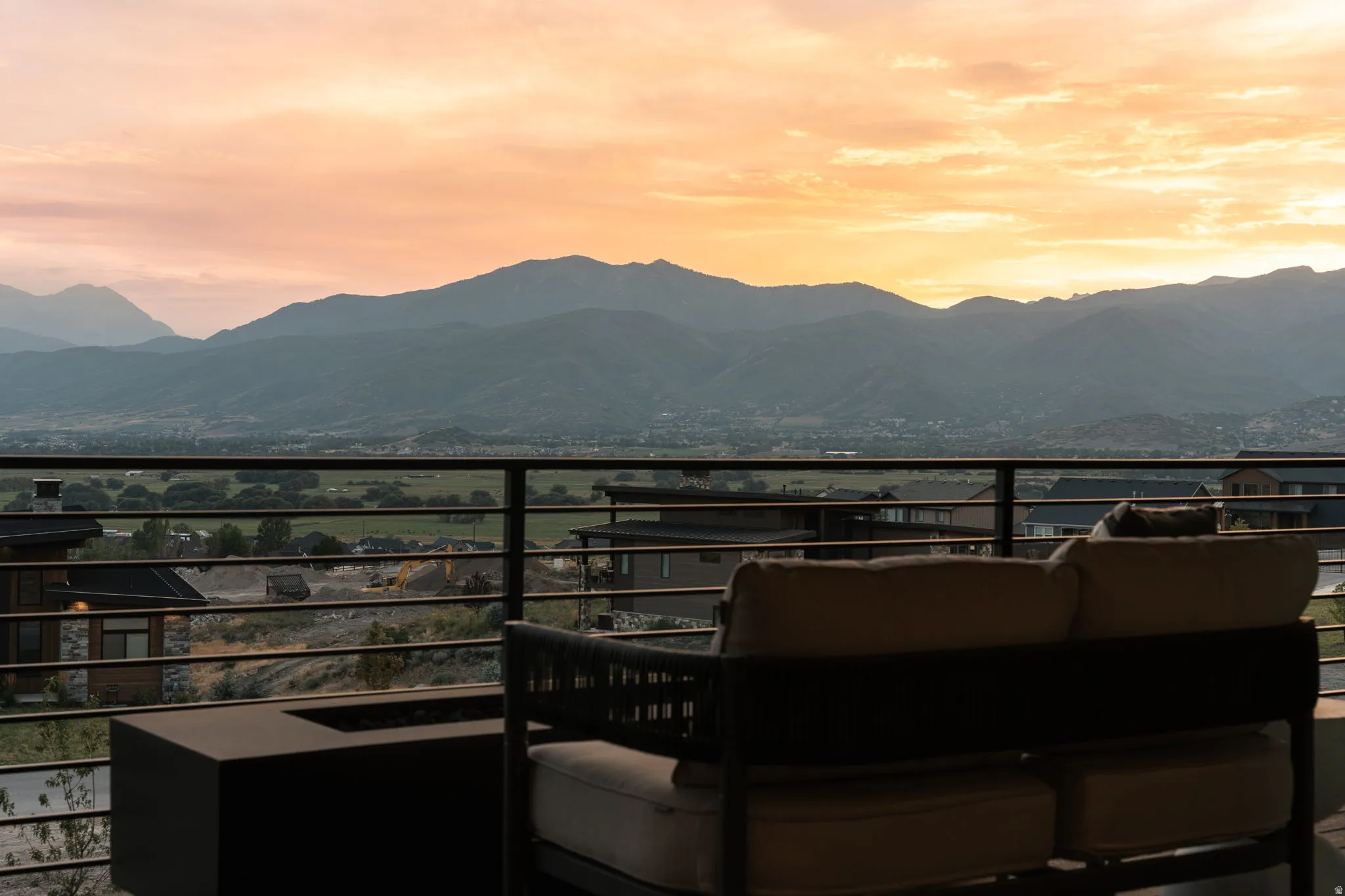 Outdoor terrace with horizontal metal railing, featuring a built-in rectangular fire pit and broad mountain scenery