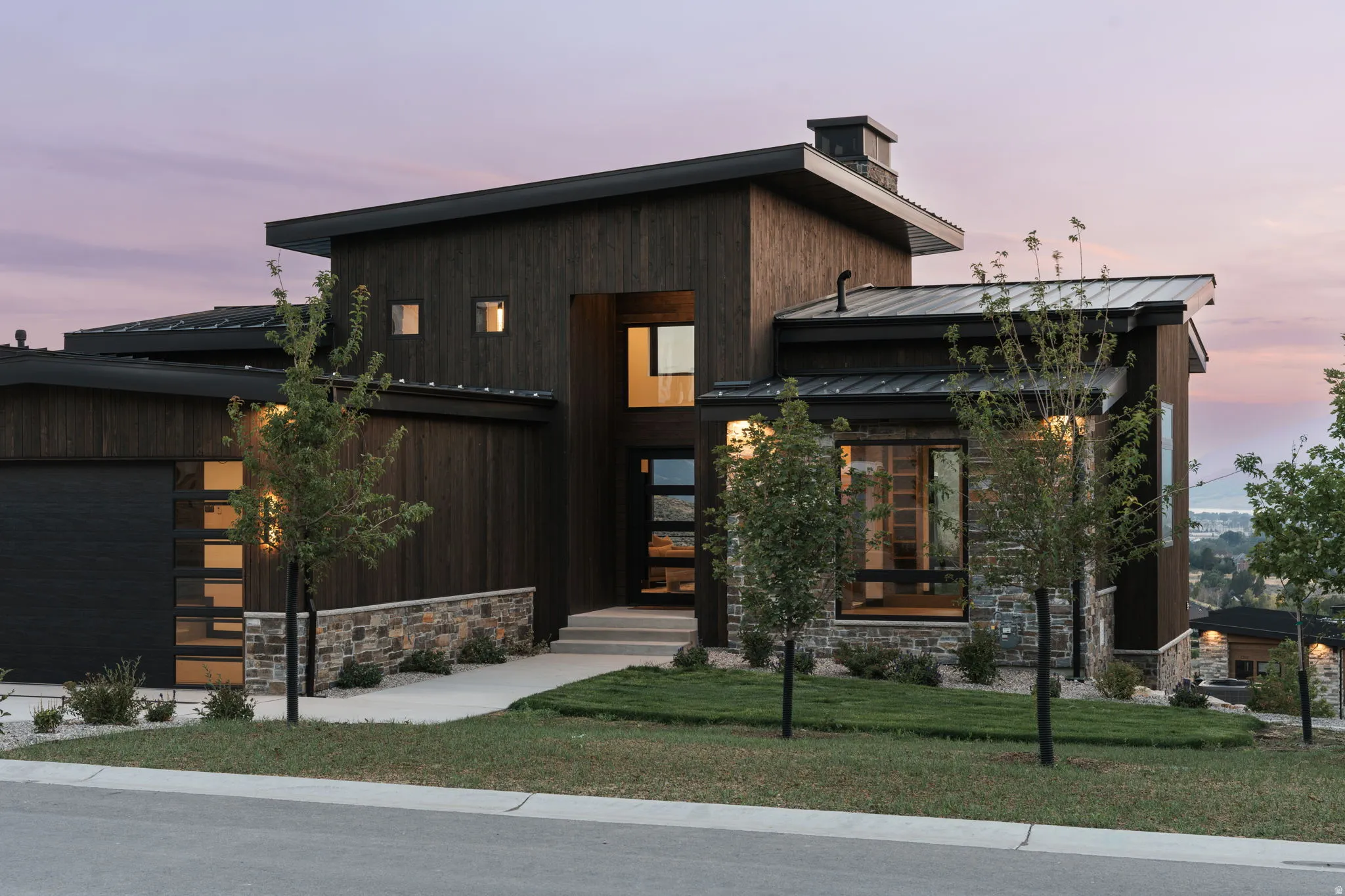 Modern architectural exterior featuring a dark wood-finish facade, natural stone accents, and a sloped metal roof
