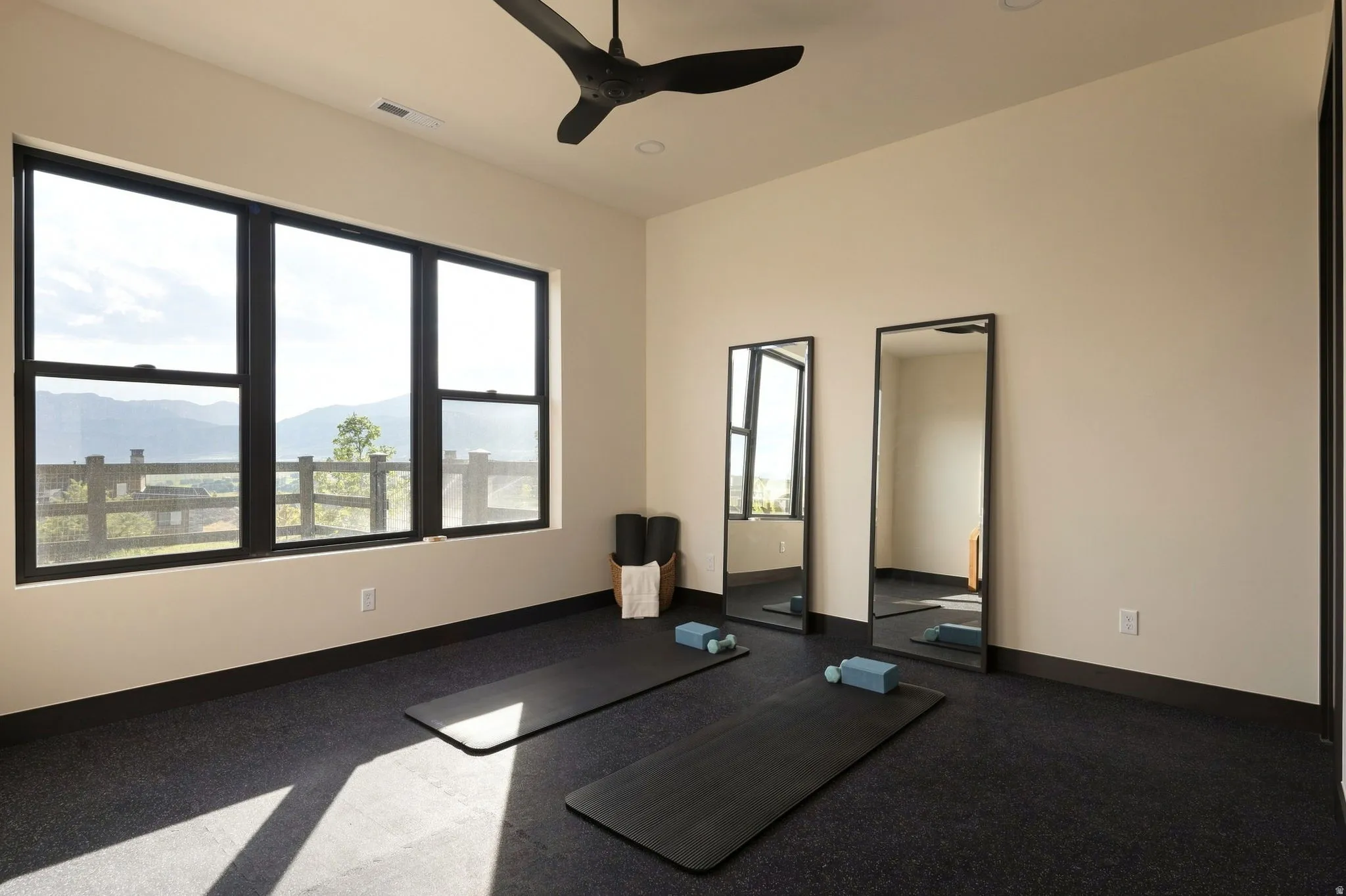 Expansive windows with mountain scenery, black-framed mirrors, a black ceiling fan, and dark flooring