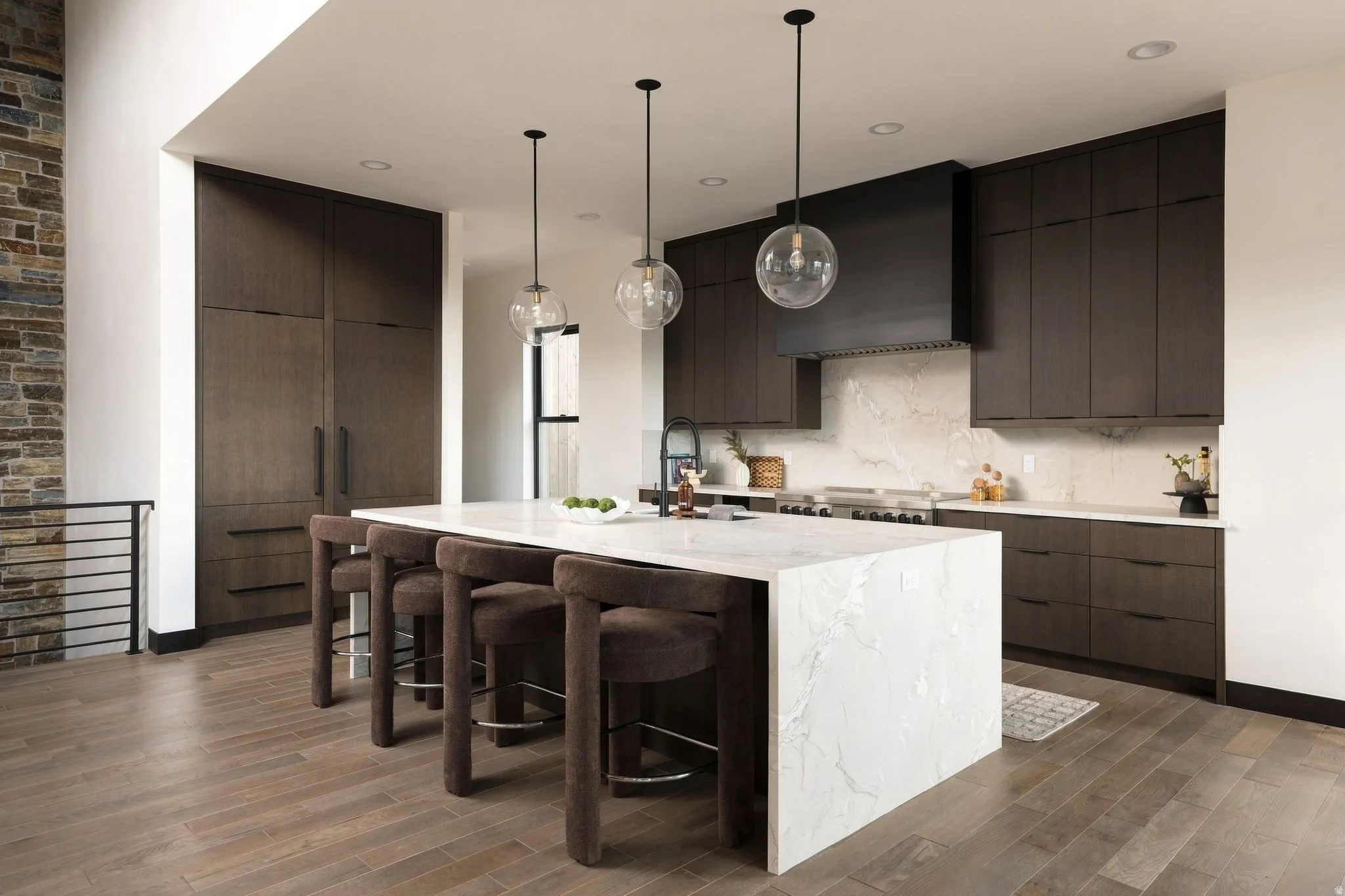 Spacious kitchen featuring a waterfall island, dark wood-finish cabinetry, integrated appliances, and a stone accent wall