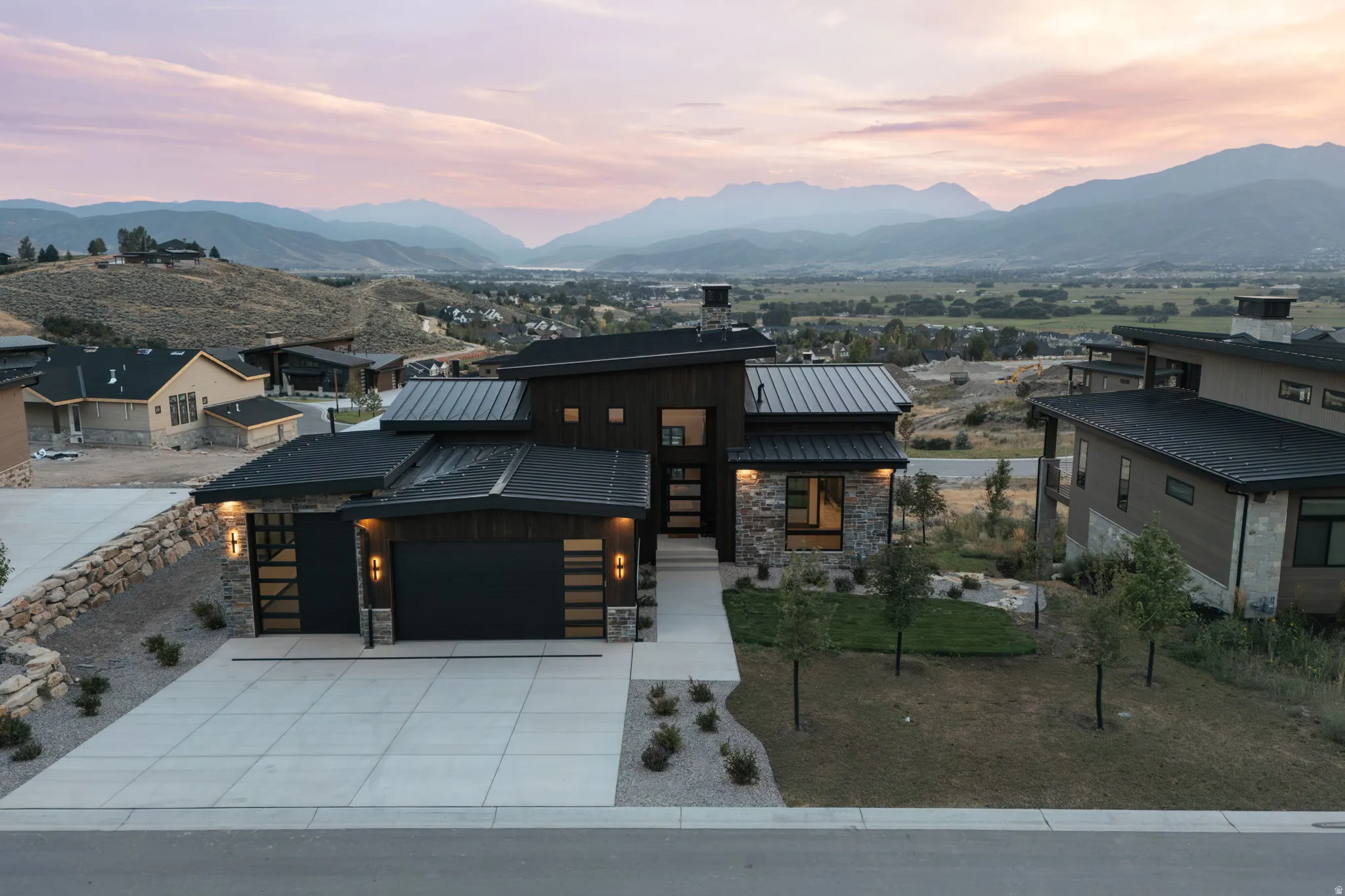 Modern architectural design featuring dark wood-look siding, stone accents, and a metal roof