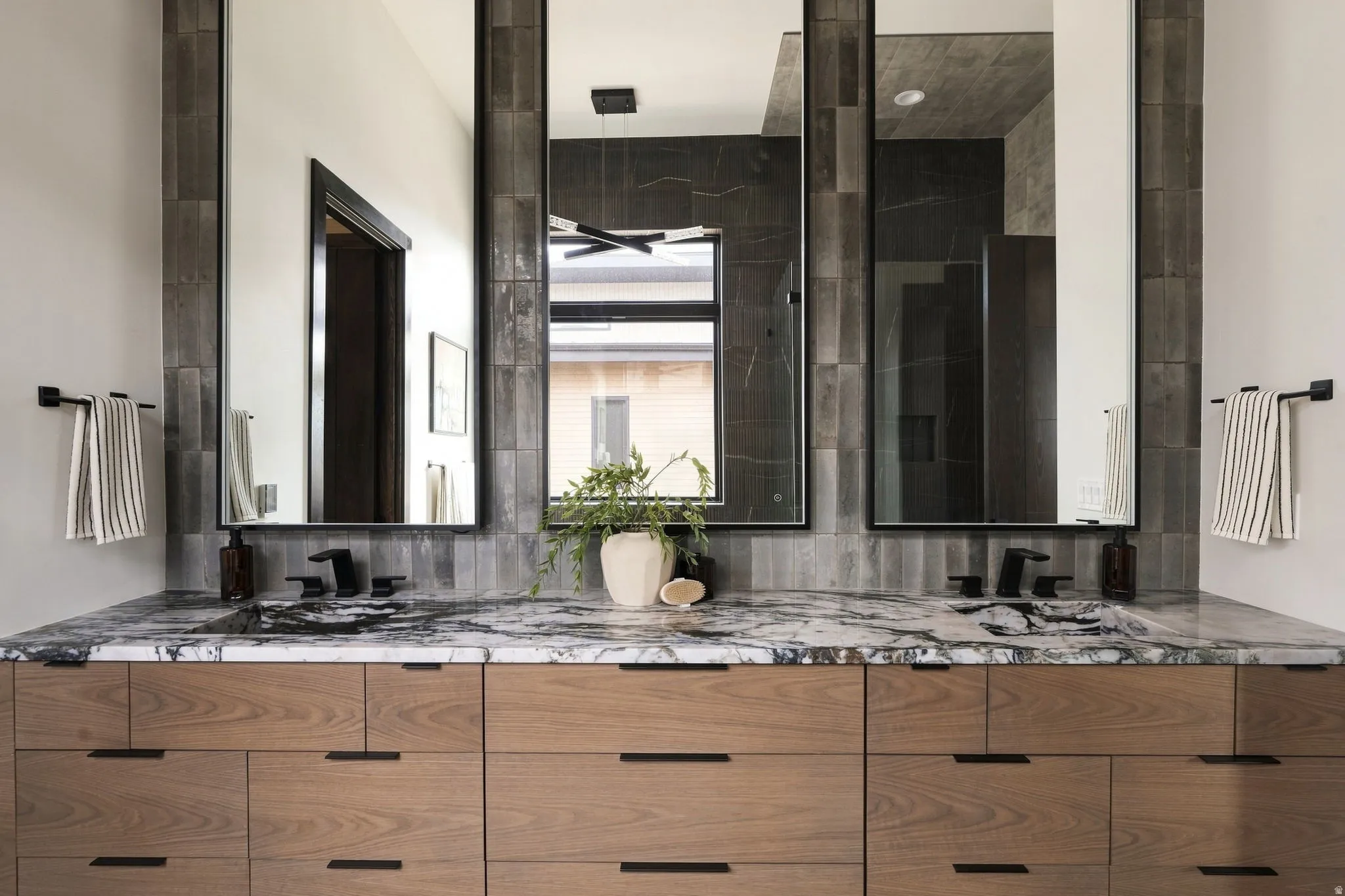 Dual vanity with wood-finish cabinetry, integrated sinks, black hardware, and slab countertops