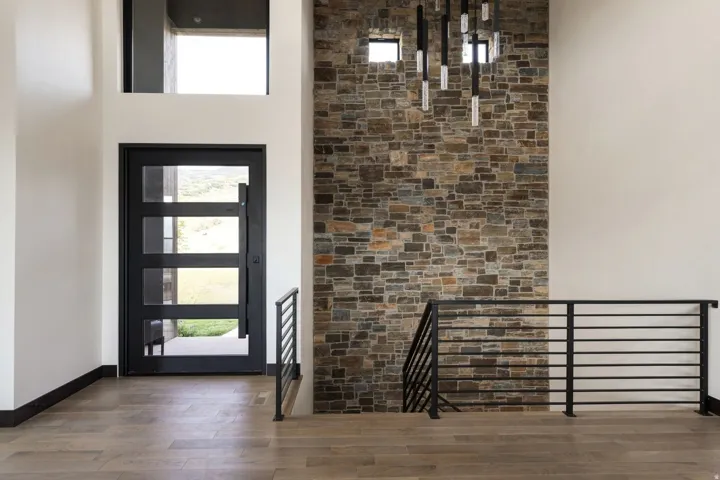 Entry foyer featuring a stone accent wall, wood-finish flooring, and a modern black entry door with frosted glass panels