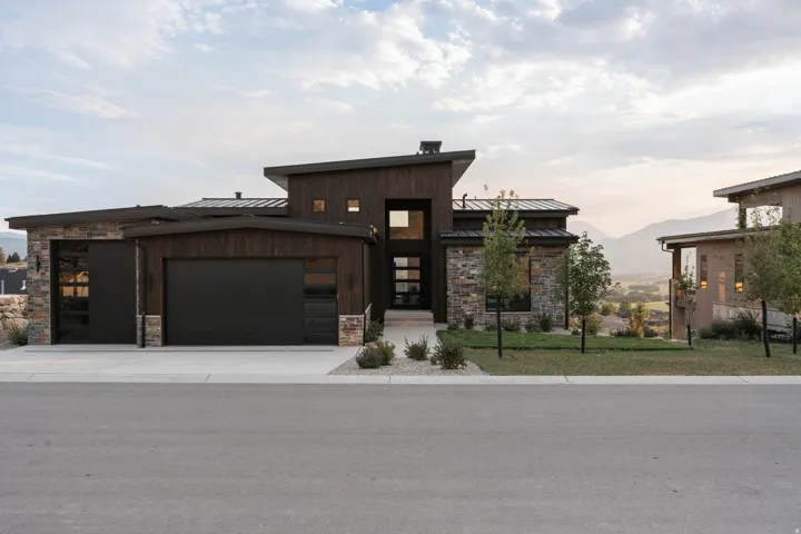 Modern architectural design featuring dark wood-finish siding, natural stone accents, a multi-paneled glass entry door, and dark garage doors with integrated window panels