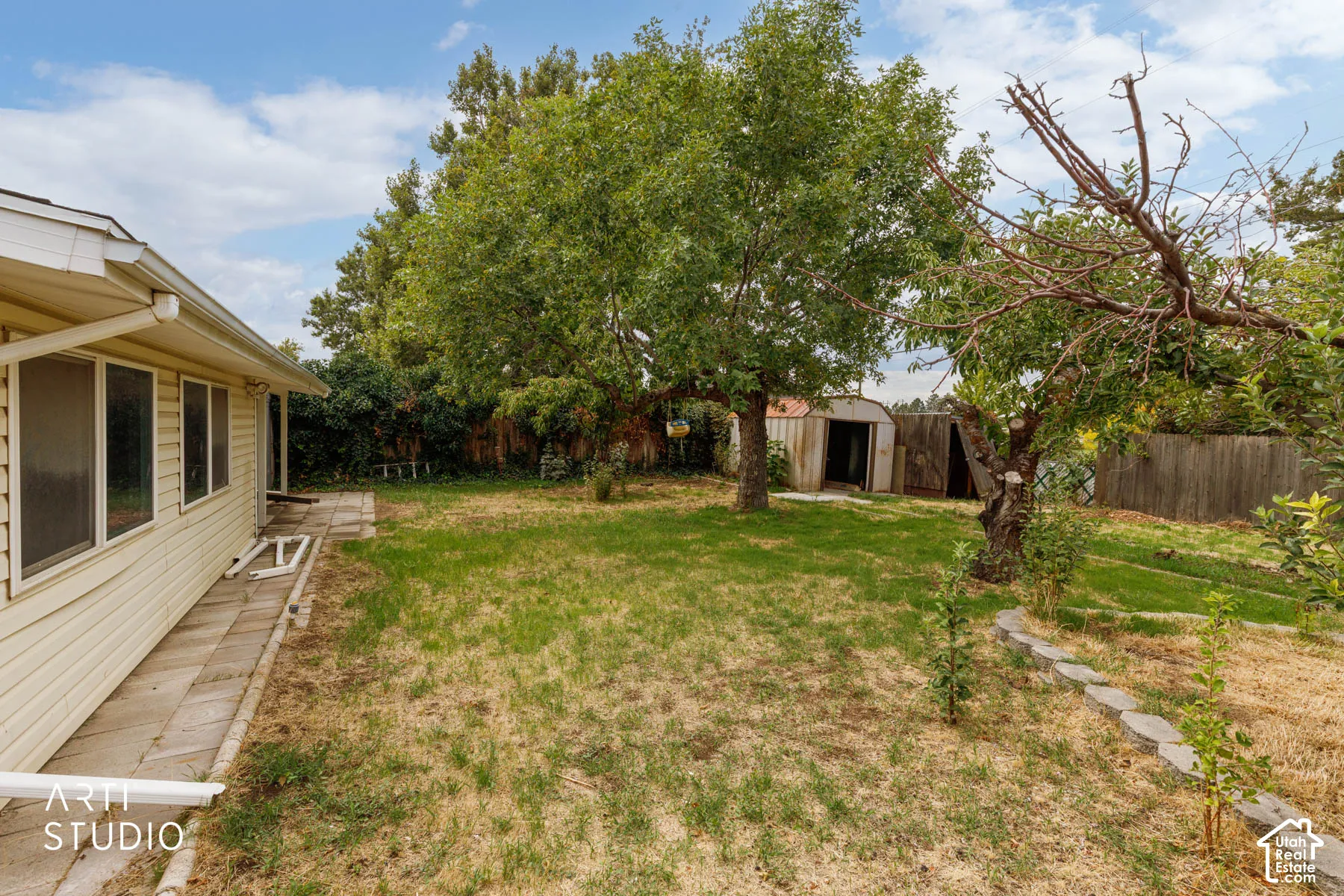 Expansive backyard featuring mature trees, a storage shed, and a privacy fence