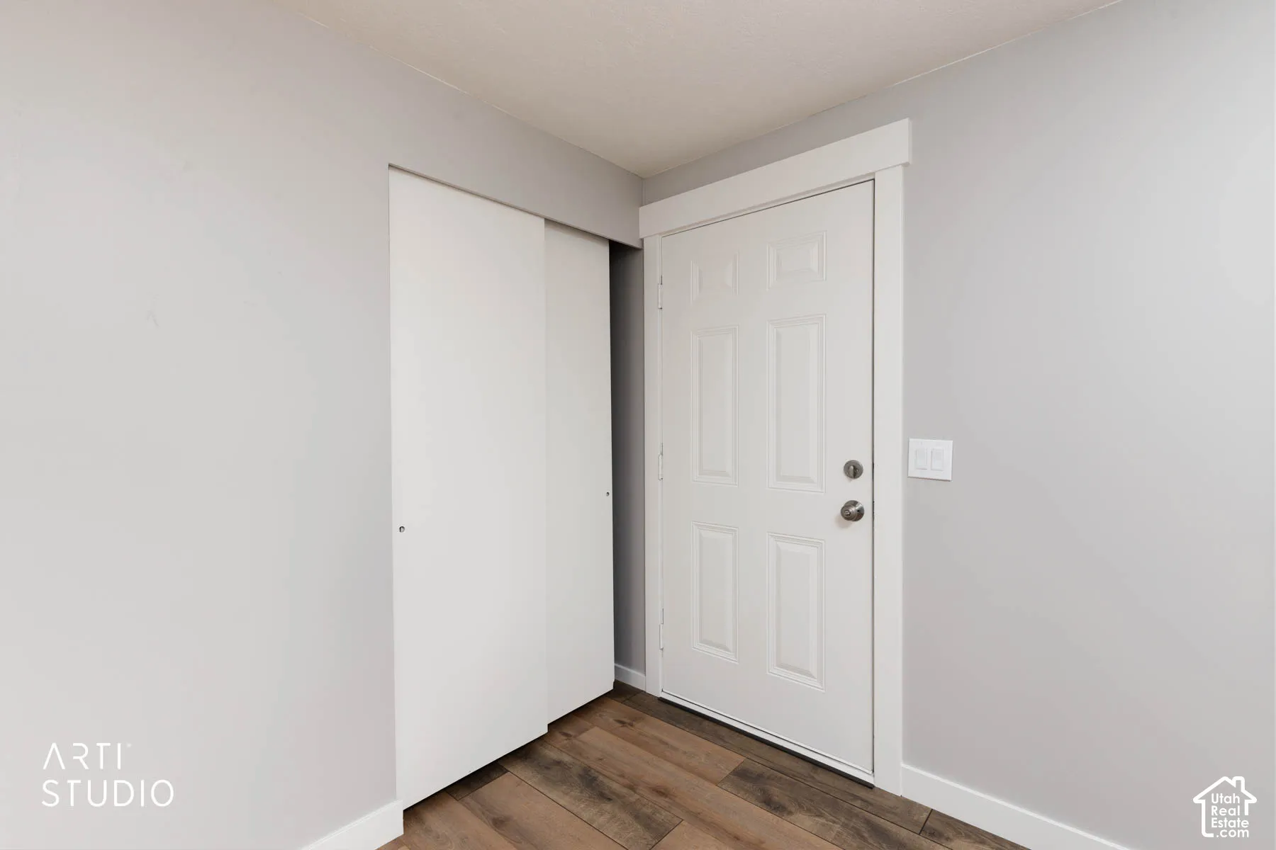 Wood-finish flooring with light gray walls, white trim, and a white paneled door
