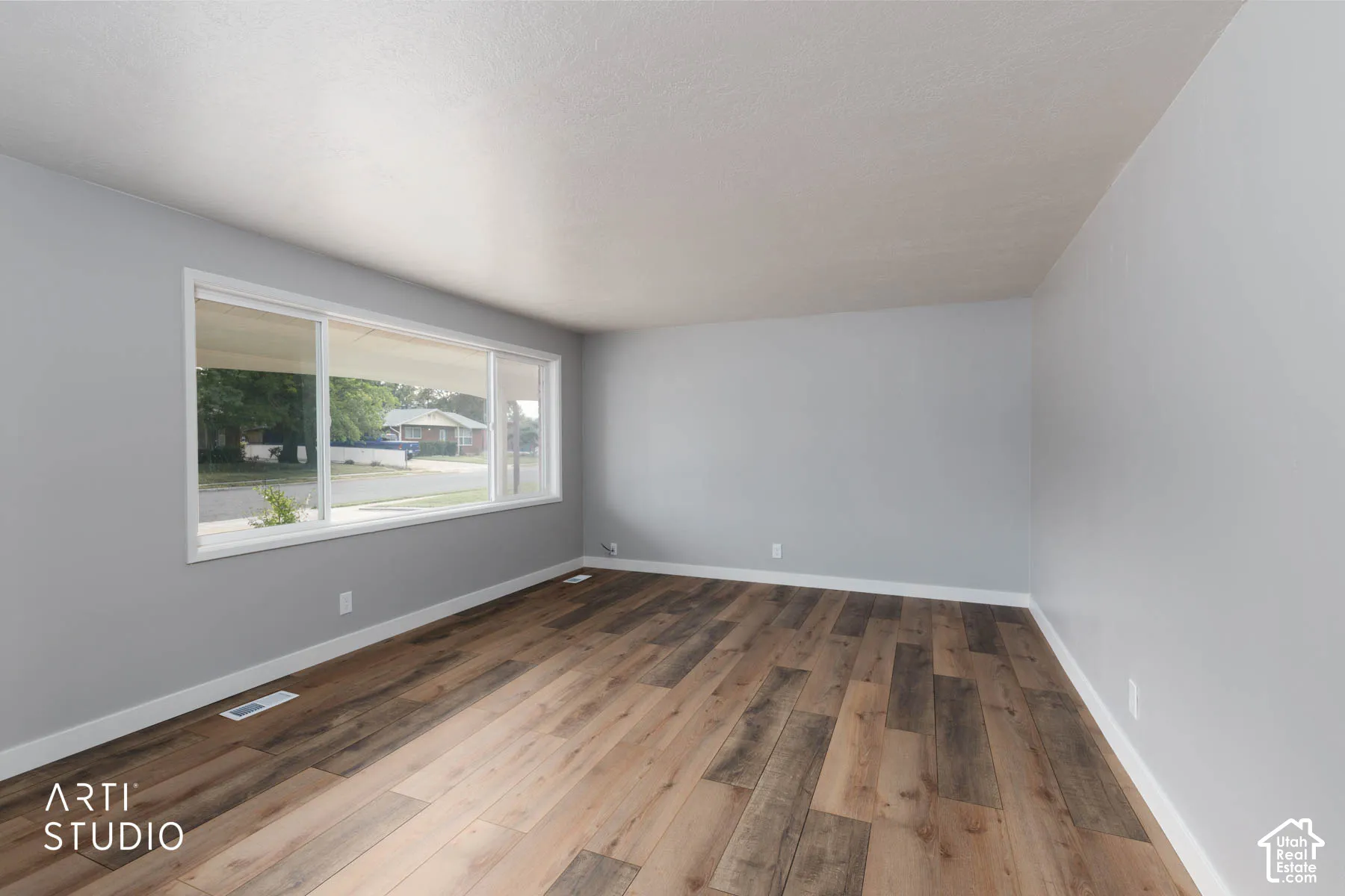 Spacious room featuring wood-finish flooring, light gray wall paint, white trim, and a large multi-pane window