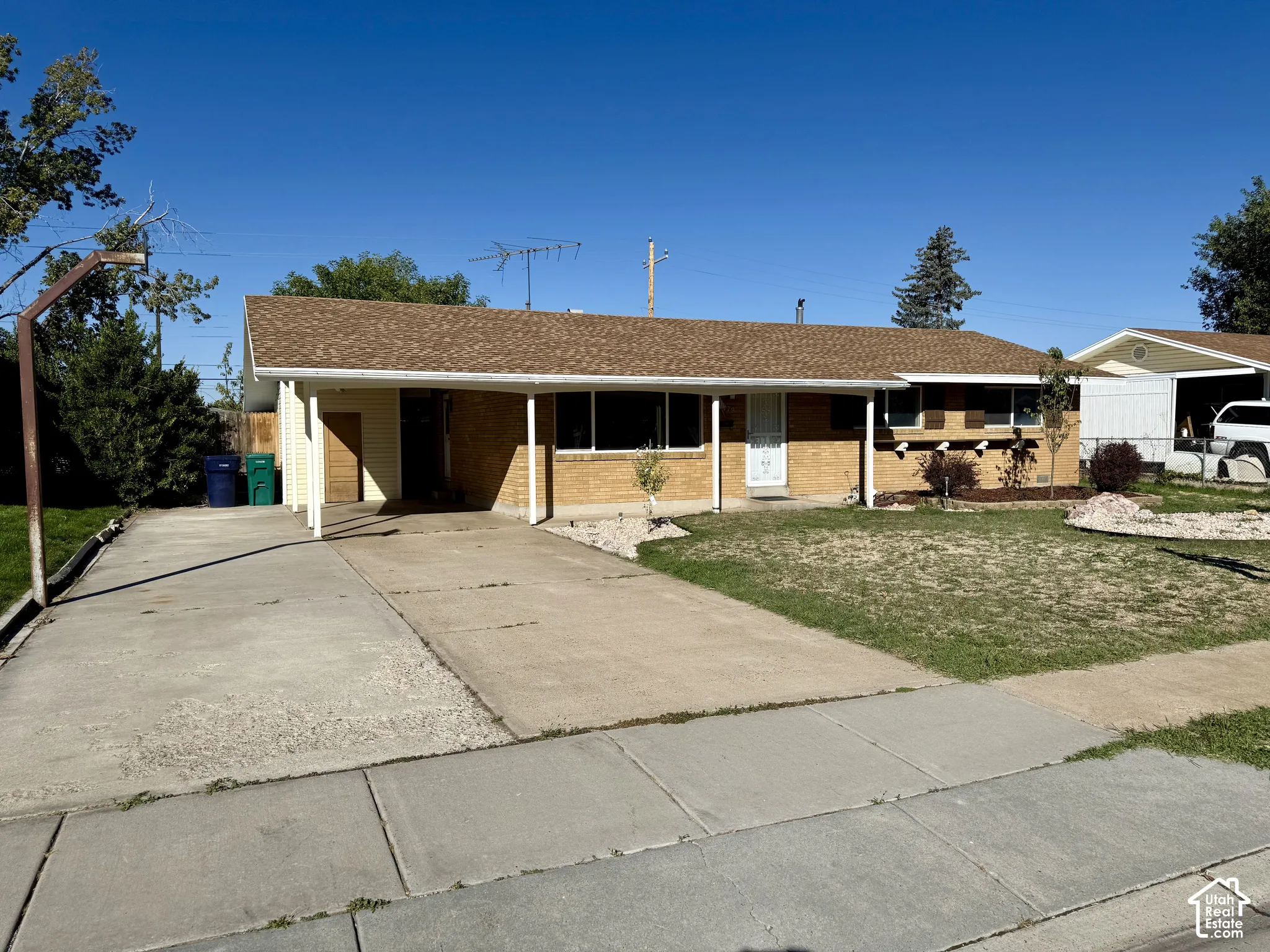 Brick facade with a covered entry, concrete driveway, and established landscaping