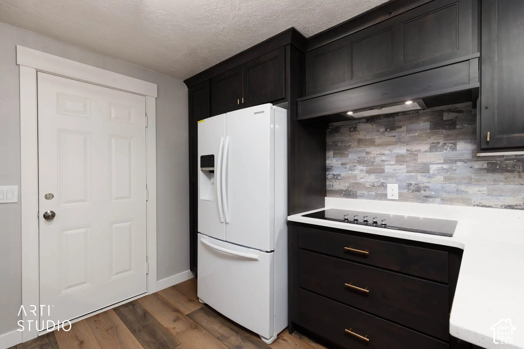 Wood-finish flooring, dark wood cabinetry, light-toned countertops, and a subway tile backsplash